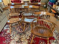 Photo showing entire set of six wooden dining chairs arranged on a patterned rug, includes two captain's chairs with arms and four armless chairs.