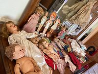 View of assortment of vintage dolls, paper dolls, and doll clothing arranged on a table showing condition and variety