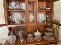 Wide view of cabinet with various crystal and china pieces inside and on the counter including crystal cake plate, candy dishes, and serving platters.