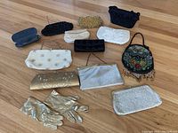Full shot of 11 small vintage clutch purses including beaded and non-beaded, pair of gold gloves, and glasses case on wood floor