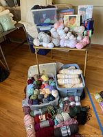 Wide view showing bins of assorted yarn skeins and balls arranged on and under table.