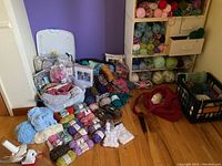 Wide shot of large yarn collection arranged on floor and shelves, including various colors and containers