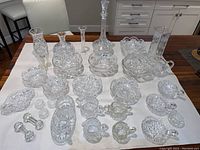 Wide shot showing entire collection of crystal glass pieces on table including decanter, vases, bowls, and small dishes