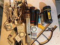 Entire lot displayed on table showing multiple extension cords, power bars, timers, flashlights in various styles and colors
