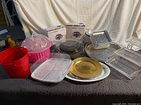 View of various serving ware items including the pink cupcake carrier, electric burners boxed in MAX packaging, assorted serving plates and containers.