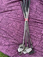 Photo of six golf clubs with steel shafts and black grips laid on a purple cloth.
