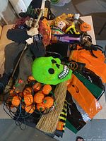 Photo showing assorted Halloween decorations including hanging kitchen witch, green skull mask, string of pumpkin lights, broom, and decorative bags.