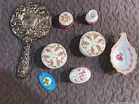 Overhead view showing all items in set including handheld mirror, white china trinket boxes with pink floral designs, small lidded containers, shell dish, tiny vase, and blue four leaf clover box