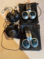 Four noise cancelling wired headphones, two Aiwa and two Sony, arranged on surface with carrying pouches visible
