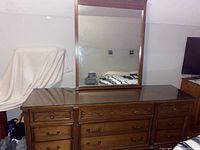 Photo of vintage wooden dresser with glass top and attached large mirror, showing the front view with all drawers and reflective glass surface.