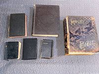 Whole lot of six old Bibles on gray quilted fabric. Includes a range of sizes with black leather or textured covers and gold embossed text on one large Bible.