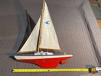 Side view of the sailboat model showing red hull, white sails, and blue bird emblem.