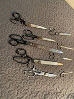 Full view of eight assorted vintage scissors arranged on a quilted surface showing black and metal handles and a range of sizes.