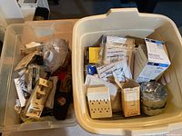Two bins containing assorted small electrical items such as battery testers, plate covers, light bulb sockets, plug adapters, and plastic electrical boxes