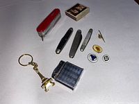 All items arranged on a flat surface: Swiss Army knife, three other pens/knives, three pins, vintage matchbox, lighter and Eiffel Tower keychain