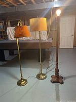 Three vintage standing lamps together on the floor, showcasing different styles and finishes.
