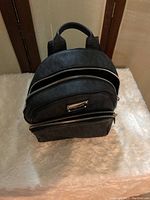 Front view of black leather backpack with two zippered compartments and silver hardware.
