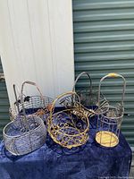 Photo showing five varied metal baskets on blue fabric backdrop, highlighting assortment and decorative metalwork patterns.