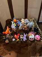 Overview of 18 assorted plush toys including Ty Beanie Babies, Teenie Beanie Babies, and Pomsies Lumies on a brown fur-like blanket.