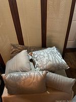 Close view of decorative accent pillows with various printed and striped patterns, mostly gray tones with scroll motifs and stripes, arranged on a chair.