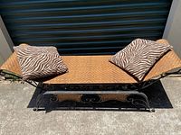 Front angled view of rattan and wrought iron curved bench with two zebra print pillows on seat.