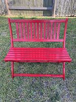 Front view of the red wooden outdoor bench showing the slatted seat and backrest on grass.