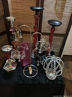 Photo showing various candleholders including acrylic bead crown candleholder, twisted red stone stem candleholders with black bases, and a silver-acrylic bead candleholder along with multicolor candleholders, all arranged on a black surface with a dark background.