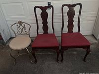 Two wooden armless chairs with red fabric seats and one metal vanity chair with beige round fabric seat in front of garage door.