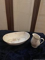 Oval serving/vegetable bowl and creamer displayed side by side on dark cloth background showing floral design and shape.