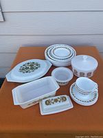 Full set of Corelle dishes stacked and grouped with vintage Pyrex and Federal milk glass pieces on orange cloth background outdoors