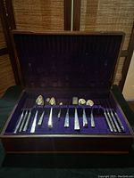 36 piece set of silverplate flatware in vintage wooden case with purple velvet interior. Top row of the box shows knives, spoons, and forks neatly arranged.