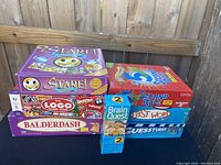 Seven board game boxes stacked in two piles: Stare, 5 Second Rule, The Logo Board Game, Balderdash, Brain Quest, Last Word, Guesstures. Photo shows titles and condition.