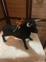 Side view of the black felt bullfighting bull figurine showing the horns, textured felt body, and colorful banderillas on the back.