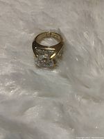 Close-up photo of yellow gold ring with large square-cut CZ solitaire and pave stones on band on a fur background.