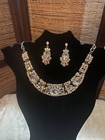 Photo of crystal embellished necklace and matching earrings displayed on black stand
