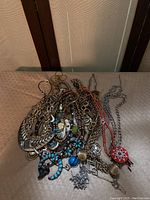 Photo showing tangled assortment of various beaded and metal costume necklaces with blue and turquoise details, circular metal links, and multiple pendant styles