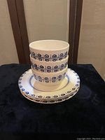 Image showing three white ceramic bowls stacked on top of two 11-inch dinner plates featuring blue circular geometric patterns on rims, placed on black cloth.