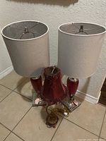 Two red glass and silver base lamps with white fabric shades about 32 inches tall, set on a tiled floor against a wall.