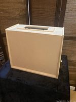 Beige hard plastic carrying case with handle on top for carrying Singer sewing machine, shown closed from side view.
