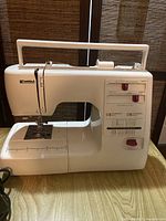 Front view of white Kenmore sewing machine with control panel and handle exposed.