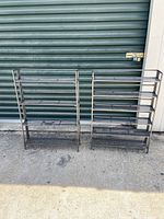 Both 4 shelf and 6 shelf antique cast iron folding racks against corrugated wall, showing size and form.