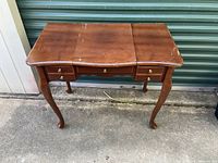 Front view of the wooden vanity table showing three sections on the tabletop and two small drawers with brass knobs.