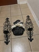 Photo showing the set laid out on the floor consisting of the wall-mounted metal vase with floral arrangement in the center and two matching metal candle sconces on either side.