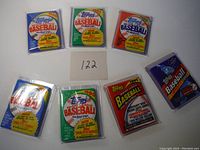 Top view of seven unopened vintage Topps Major League Baseball wax packs from 1986 to 1991 in protective plastic, arranged in an arc around a card labeled '122'.