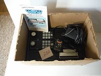 Top view of ColecoVision console, controllers, manual, and power adapter inside a cardboard box, showing all items together.