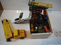 Overview of box full of die cast cars and trucks, showing various vehicles including a yellow bus and white racing car.