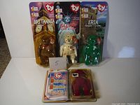Three Beanie Babies in blister card packaging visible: Britannia the Bear, Glory the Bear, Erin the Bear, each with distinct colors and flags on plush bodies.