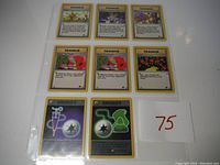 Eight Pokémon cards from the Team Rocket set including six Trainer cards and two Energy cards laid out inside a protective sleeve.