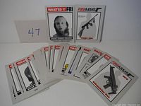 Set of collectible cards laid out, featuring portraits of FBI Most Wanted individuals and firearms illustrations.