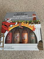 Front view of the box showing 4 bottles of hot sauce with Santa illustration and fire graphics.